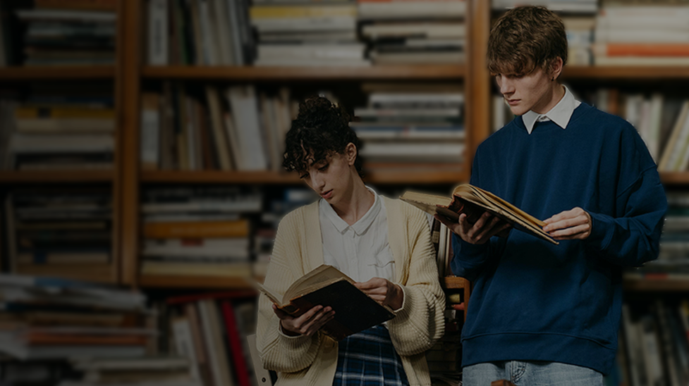 Dwójka młodych osób stoi na tle półek wypełnionych książkami. Studentka w jasnym swetrze i koszuli trzyma otwartą książkę i skupia się na czytaniu. Obok niej stoi student w niebieskiej bluzie i jasnych dżinsach, również pochłonięty lekturą. Tło tworzy biblioteczna ściana pełna książek.