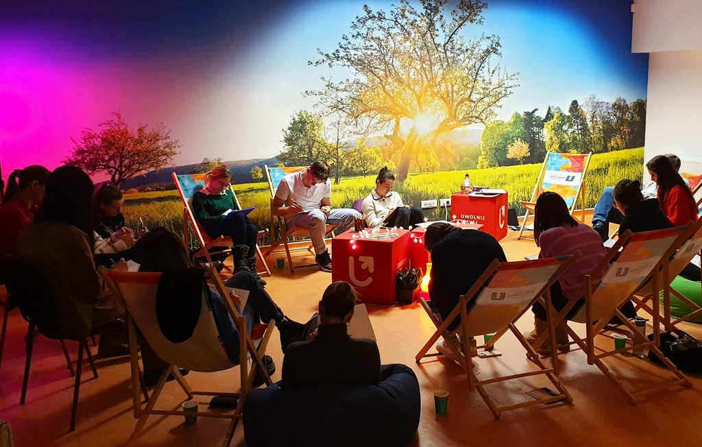 grupa osób siedząca na leżakach w przyciemnionej sali szkoleniowej