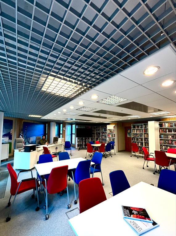 American Corner Łódź. Na pierwszym planie stoły i czerwone oraz niebieskie krzesła.