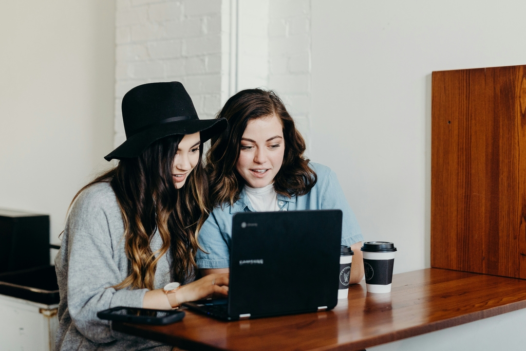A decorative element: two smiling women looking at a laptop screen
