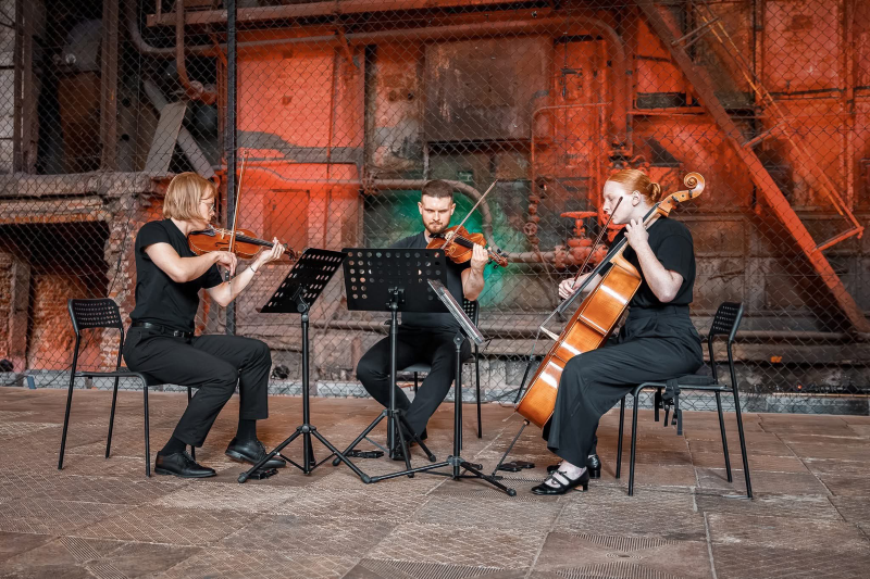 The photo shows three people playing string instruments