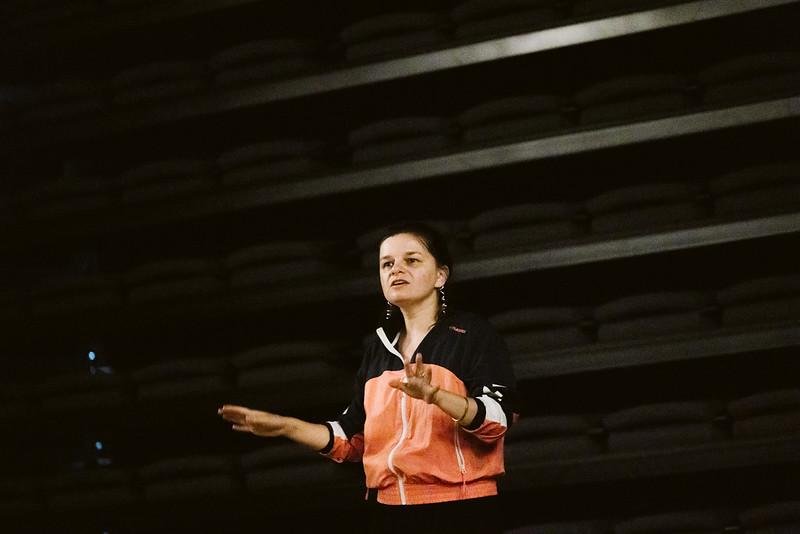 Na zdjęciu widoczna jest kobieta stojąca na tle ciemnej ściany.