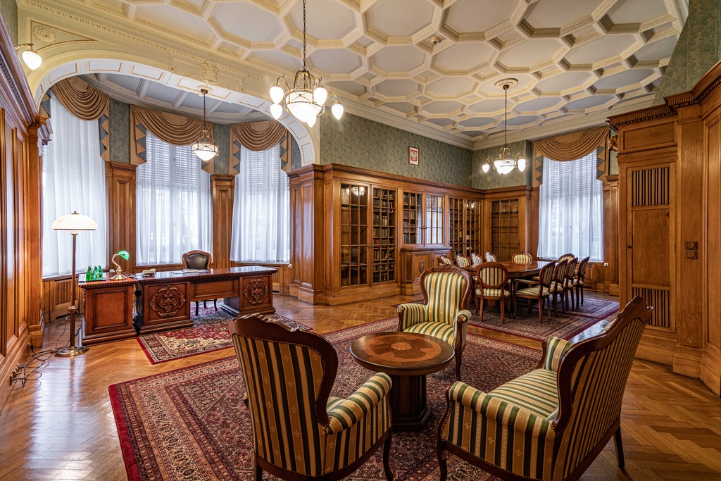 wnętrze gabinetu m.in biurko, szafy biblioteczne i stolik z krzesłami