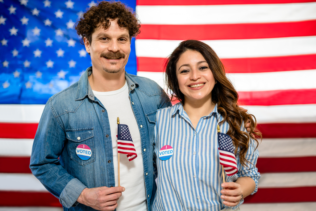 Kobieta i mężczyzna zachęcający do udziału w wyborach na tle amerykańskiej flagi.