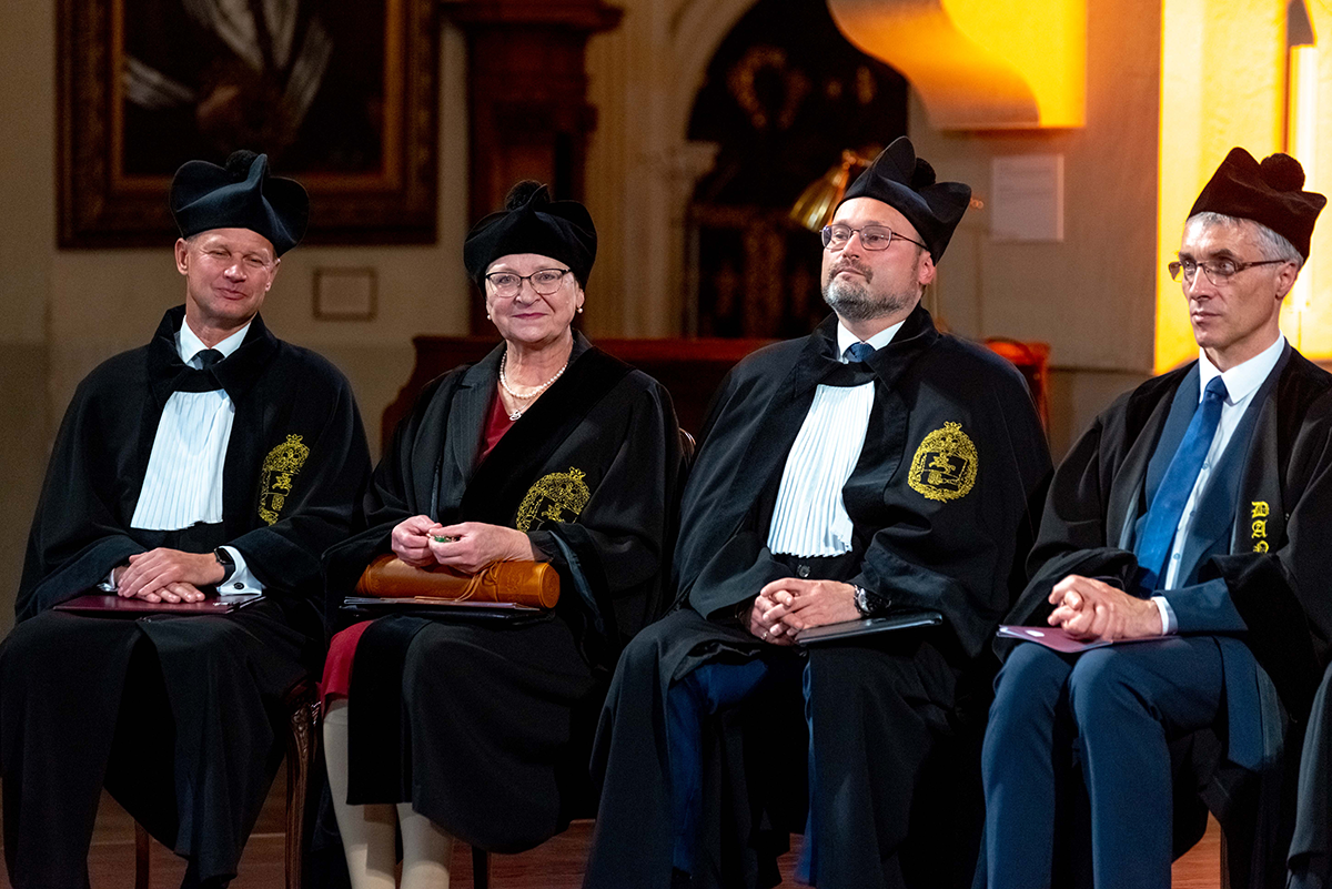 Jedna kobieta i trzech mężczyzn w uniwersyteckich togach.