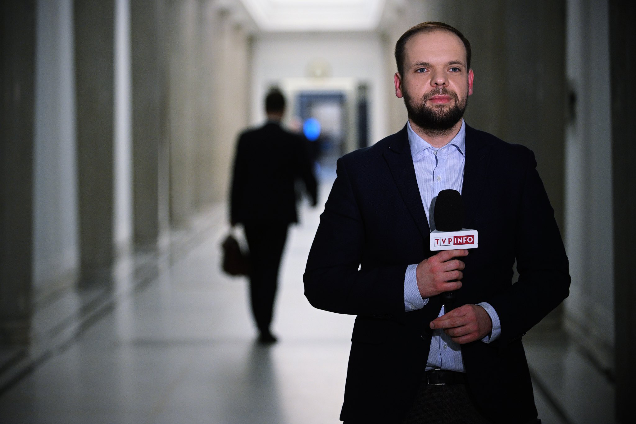 Roch Kowalski - mężczyzna w marynarce, z brodą, trzymający mikrofon reporterki