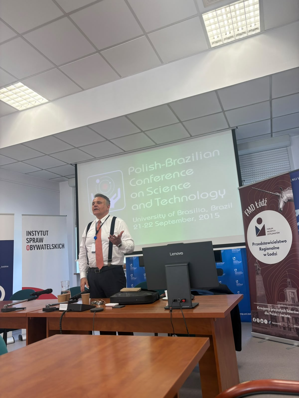 Osoba stojąca przy stole konferencyjnym wygłasza prezentację w sali wykładowej; za plecami widoczny jest ekran z napisem „Polish-Brazilian Conference on Science and Technology, University of Brasilia, Brazil, 21–22 September, 2015”. Na stole znajdują się mikrofony, komputer Lenovo oraz akcesoria, a po bokach ustawione są roll-upy, w tym „Instytut Spraw Obywatelskich” oraz „FMD Łódź – Przedstawicielstwo Regionalne w Łodzi”. Osoba stojąca przy stole konferencyjnym wygłasza prezentację w sali wykładowej; za plecami widoczny jest ekran z napisem „Polish-Brazilian Conference on Science and Technology, University of Brasilia, Brazil, 21–22 September, 2015”. Na stole znajdują się mikrofony, komputer Lenovo oraz akcesoria, a po bokach ustawione są roll-upy, w tym „Instytut Spraw Obywatelskich” oraz „FMD Łódź – Przedstawicielstwo Regionalne w Łodzi”.