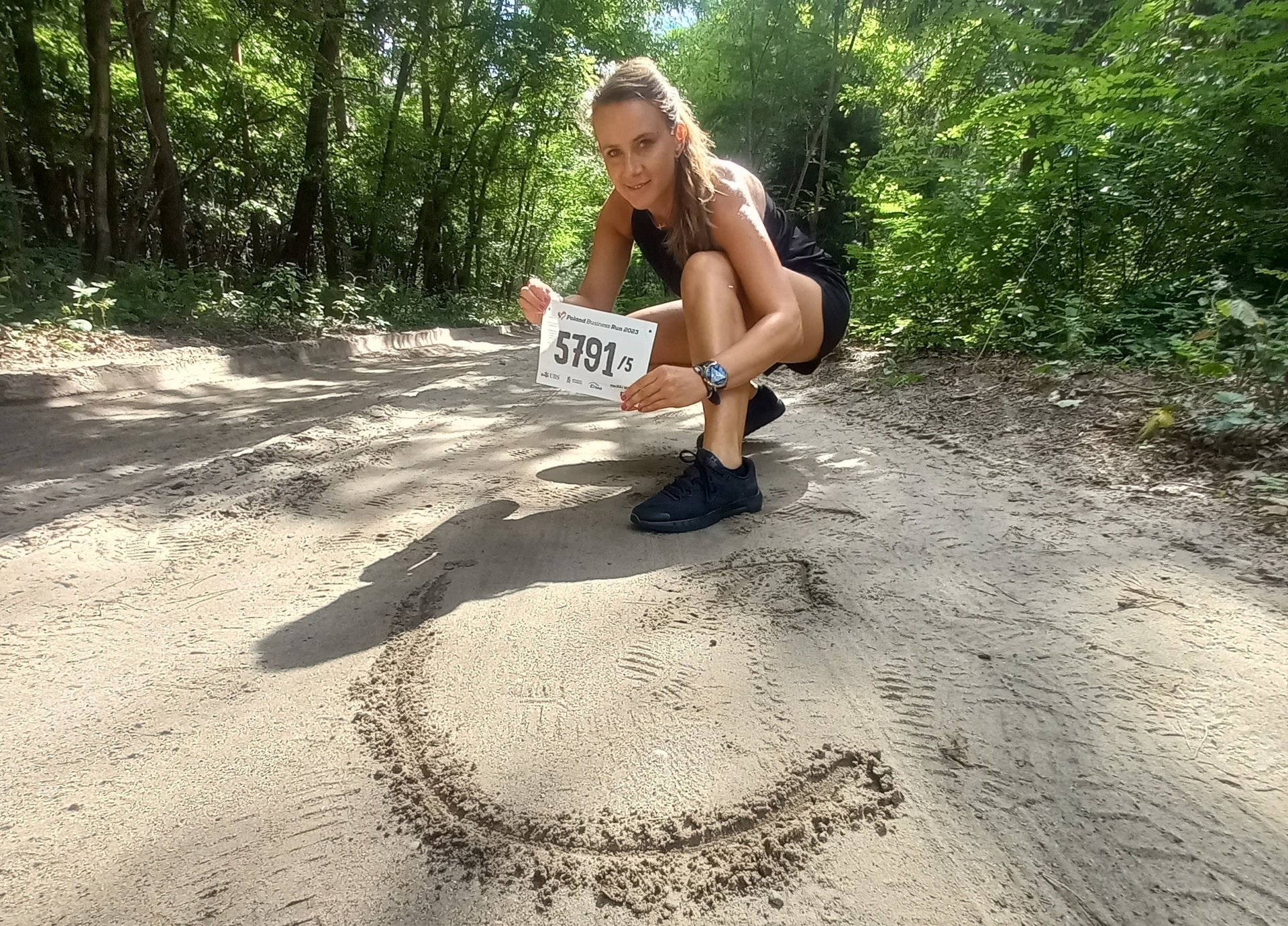female participant of the run in the park and the logo of the University of Lodz which is written on the sandy road