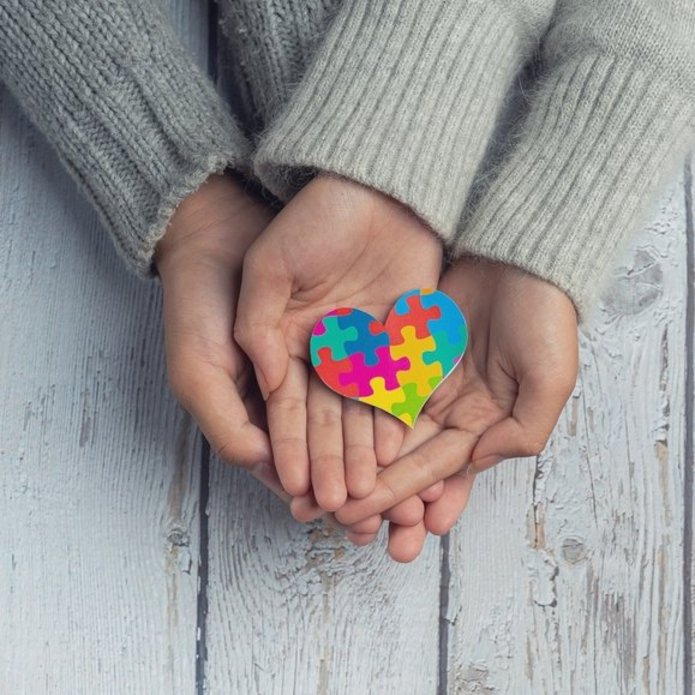zbliżenie na dwie pary dłoni na których leży serce z kolorowych puzzli