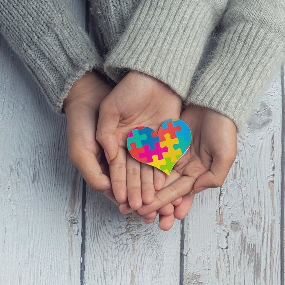zbliżenie na dwie pary dłoni na których leży serce z kolorowych puzzli