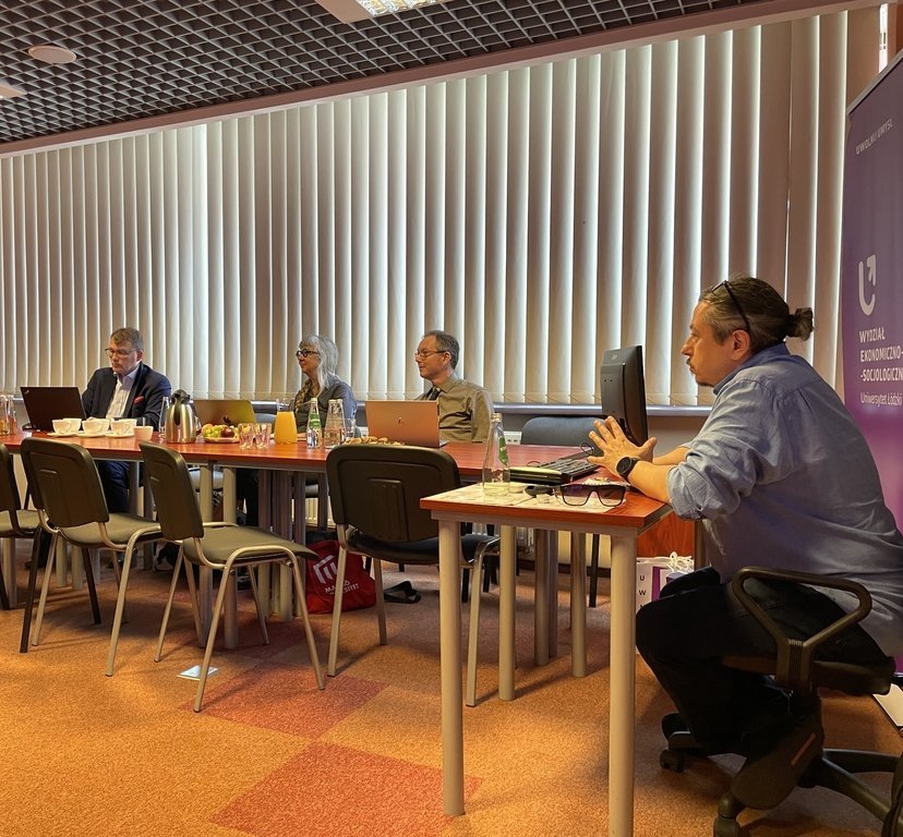 grupa ludzi siedząca przy stołach z poczęstunkiem i laptopami