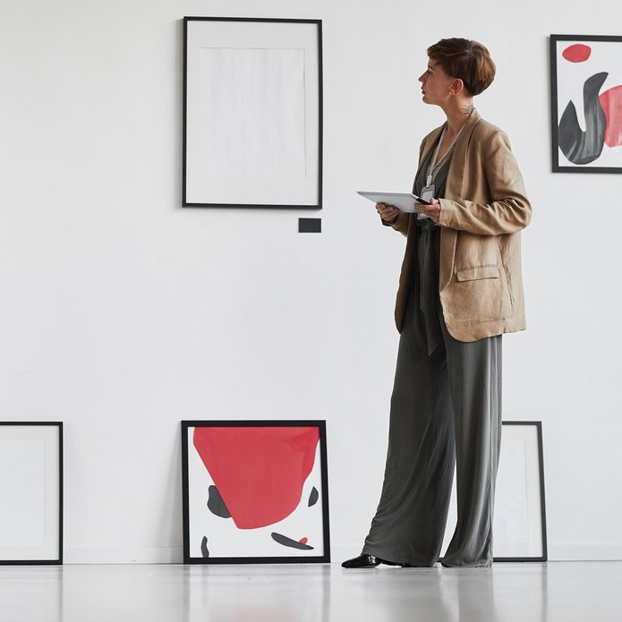 a decorative element: a decorative element: a woman looking at works of art hanging on the wall and standing on the floor