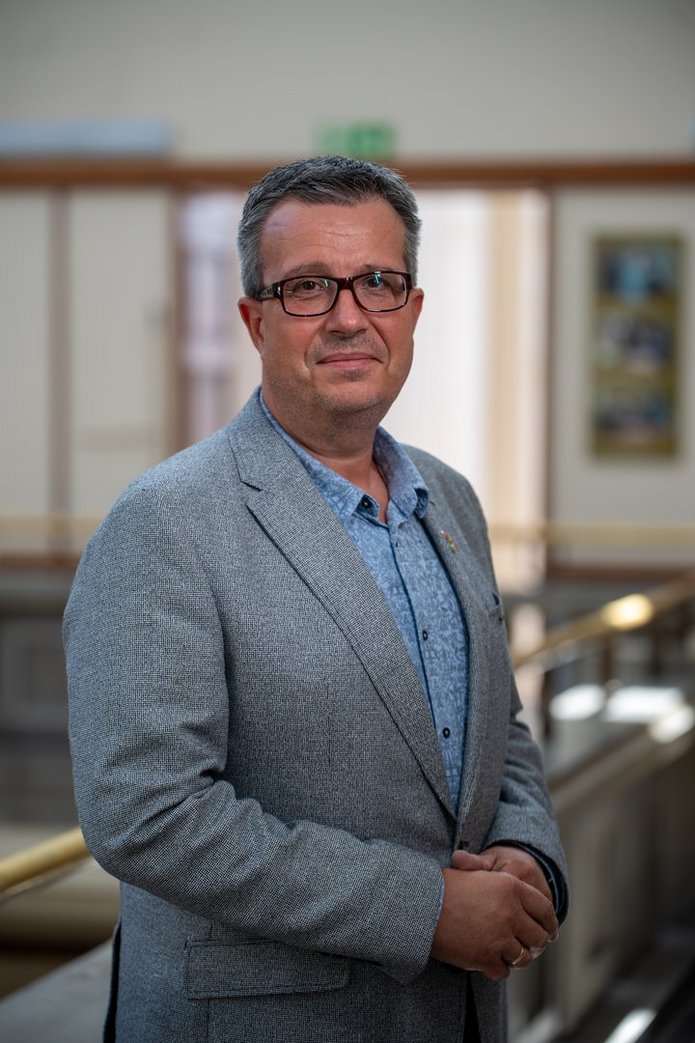 [Translate to English:] Mężczyzna stoi przodem do aparatu, ubrany w garnitur. 