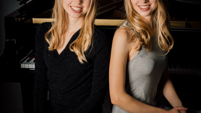 A photo of two blonde sisters sitting at the piano