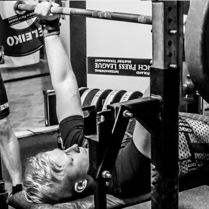 Mężczyzna z niepełnosprawnością podnosi sztangę leżąc