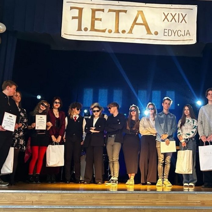 młodzi ludzie stoją na scenie pod banerem z hasłem FETA