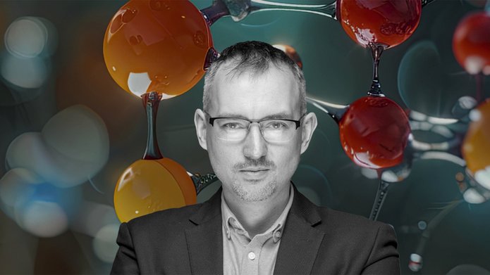 Zdjęcie portretowe dra hab. Łukasza Półtoraka, prof. UŁ na tle kulek symbolizujących molekuły
