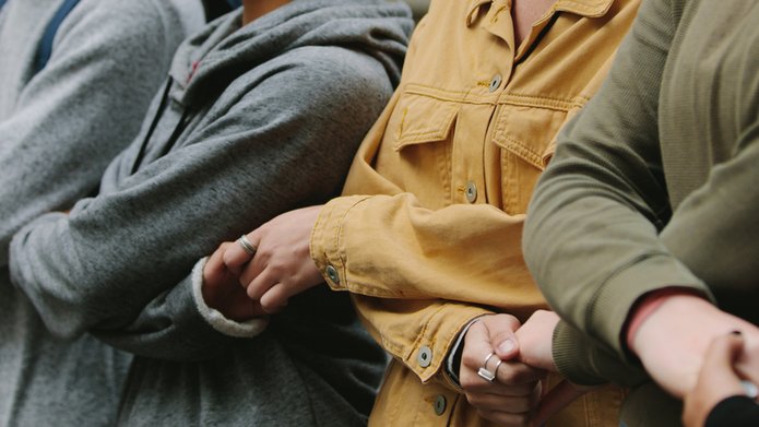 Sylwetki 4 osób stojących obok siebie i trzymających się za skrzyżowane ręce