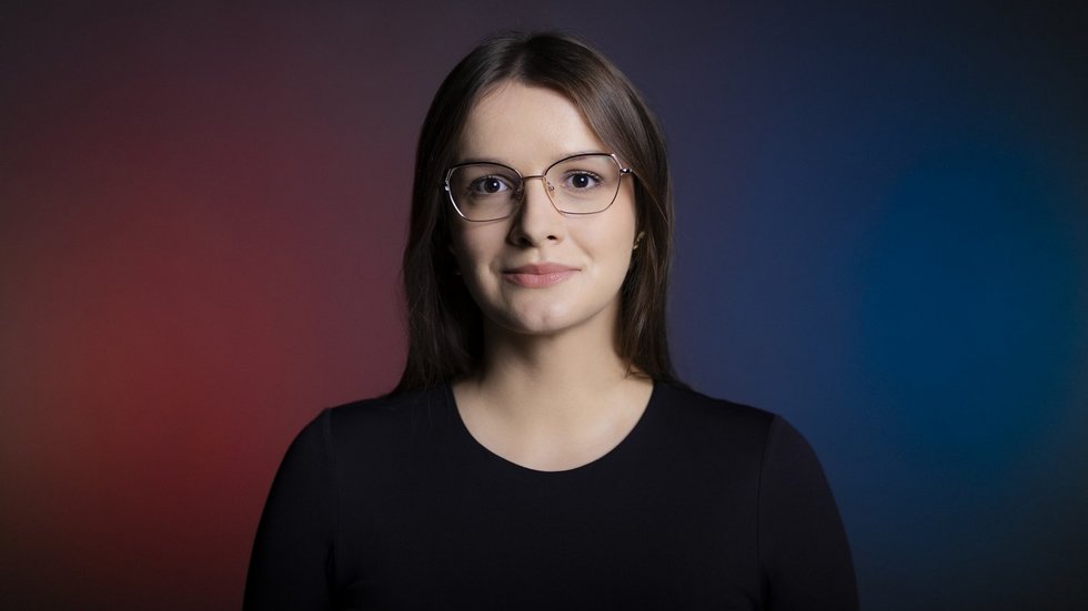 Dziewczyna z długimi brązowymi włosami na tle fioletowo granatowej ściany