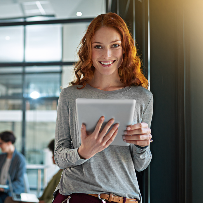 a smiling woman with red curly hair who is holding a tablet