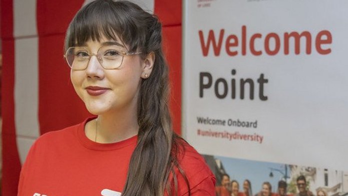 Dziewczyna w czerwonej koszulce UŁ stoi na tle plakatu z napisem "Welcome Point"