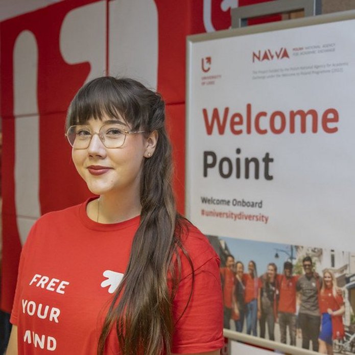 Dziewczyna w czerwonej koszulce UŁ stoi na tle plakatu z napisem "Welcome Point"