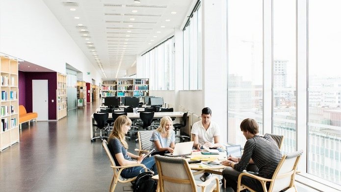 Grupa studentów w jasnym pomieszczeniu pracuje nad projektem 