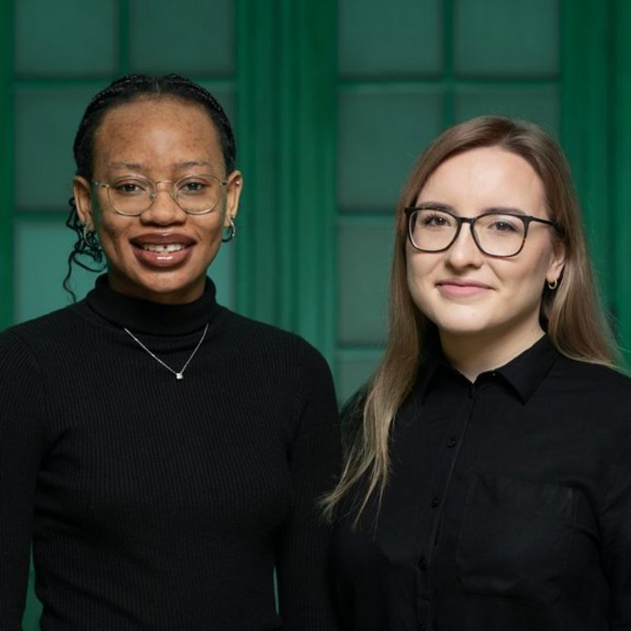 Zdjęcie Julity Maciejewskiej i Rumbidzai Hodzong. Dwie dziewczyny stoją obok siebie, są ubrane na czarno.