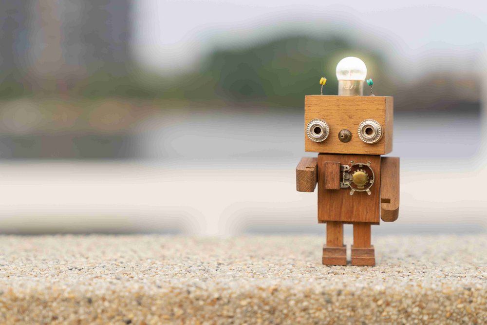 Little retro wood robot with light bulb on the head standing on the table.