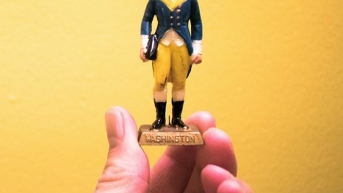 A hand holding a figurine of George Washington