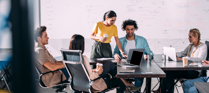 grupa młodych osób podczas spotkania patrzy na komputer i prowadzi rozmowy