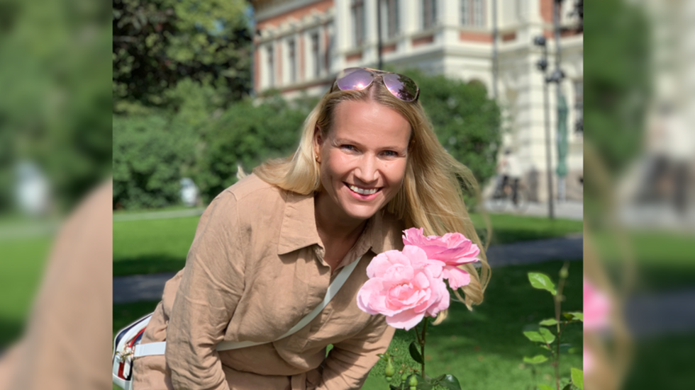 Prof. Marjaana Kangas smiling, posing next to a rose flower
