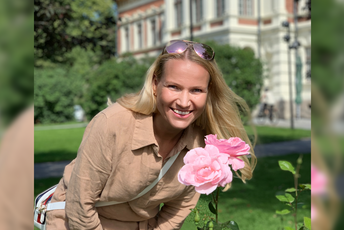 Prof. Marjaana Kangas smiling, posing next to a rose flower