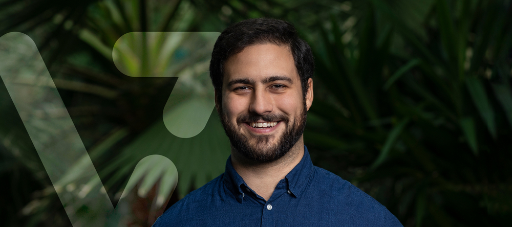 uśmiechnięty dr Naziris obok grafiki przypominającej literę V uśmiechnięty dr Naziris obok grafiki przypominającej literę V