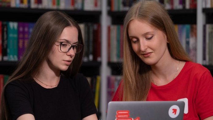 dwie studencki siedzą w bibliotece przy laptopie i dyskutują 
