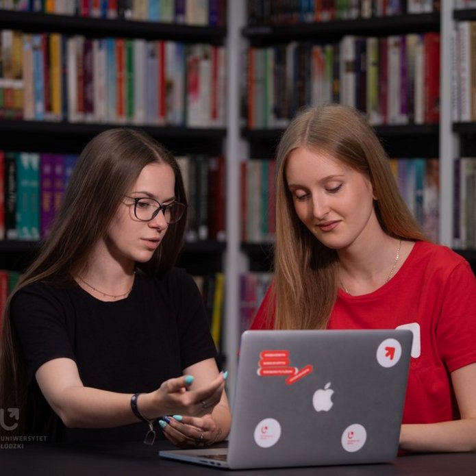 dwie studencki siedzą w bibliotece przy laptopie i dyskutują 