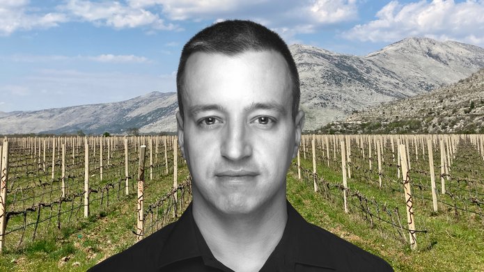 Dr Marek Majer against the background of a field of short-cut vines. Mountains in the background.