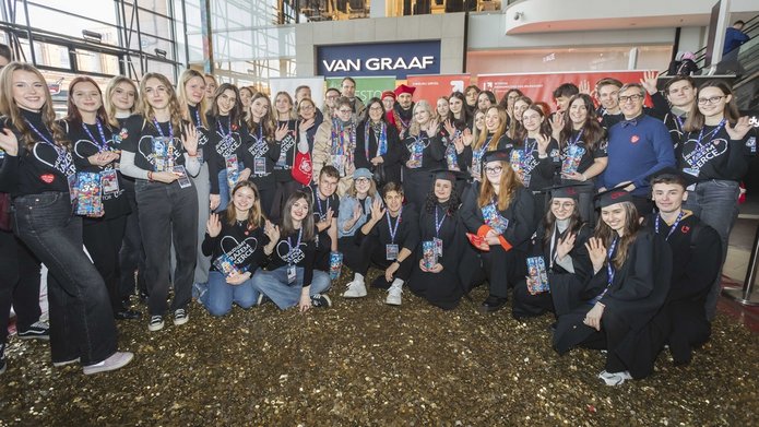 Grupa kilkudziesięciu osób stojąca na wielkim sercu z monet