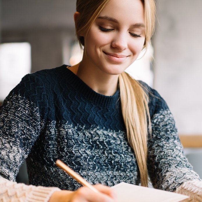 Kobieta w granatowym swetrze robiąca notatatki