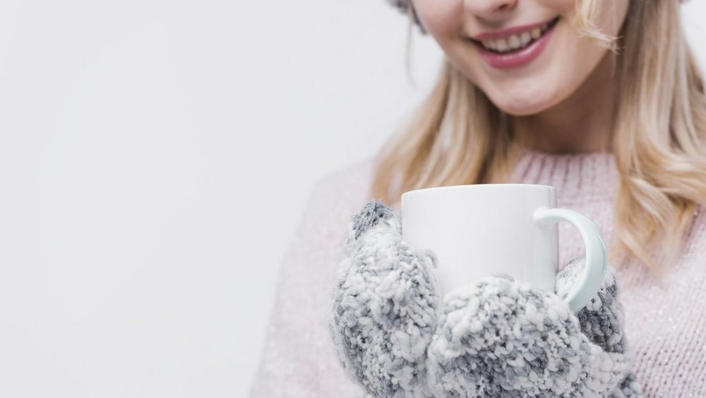 Zdjęcie: uśmiechnięta młoda kobieta w ciepłych rękawiczkach trzyma kubek