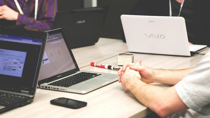 Widok na biurko z otwartymi laptopami, widoczna osoba z boku