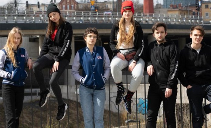 młodzi ludzie stoją przy płocie dworca