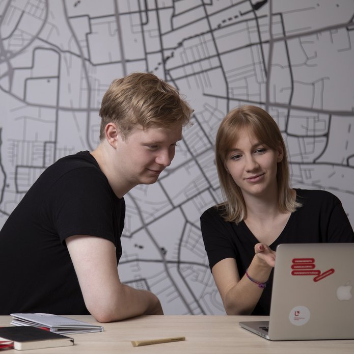 Male and female students in black t-shirts sitting at a table and looking at a computer