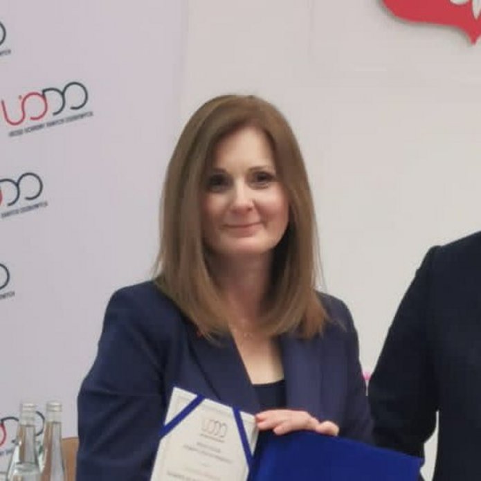 Kobieta w żakiecie odbierająca nagrodę od mężczyzny w ganiturze