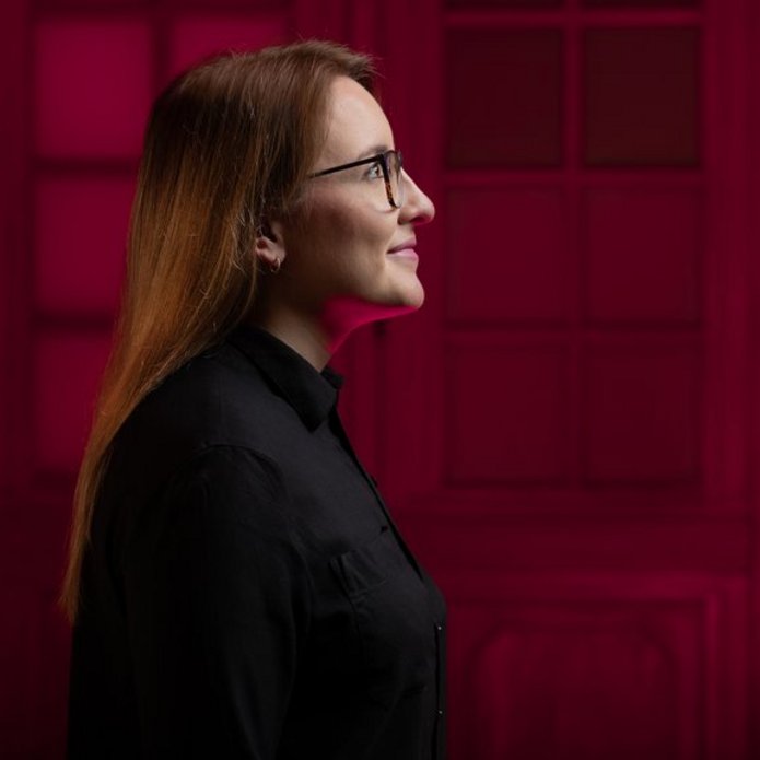 Zdjęcie przedstawia profil studentki na czerwonym tle.