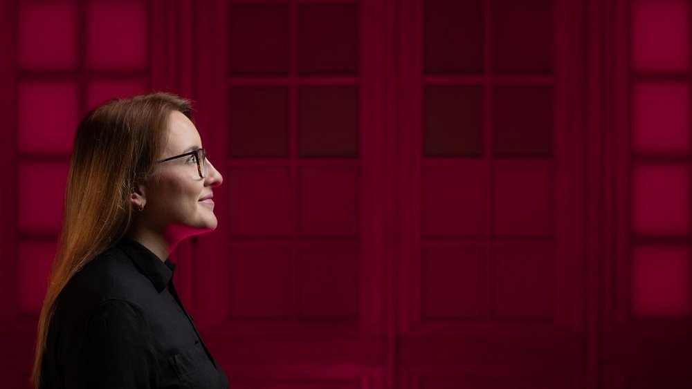 Zdjęcie przedstawia profil studentki na czerwonym tle.