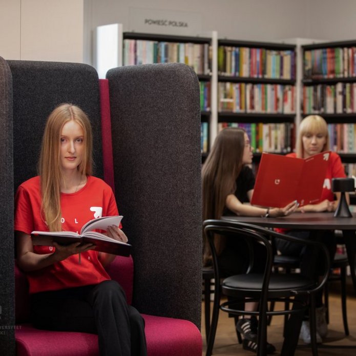 studenci w czytelni, jedna dziewczyna siedzi w fotelu, 3 osoby przy stole
