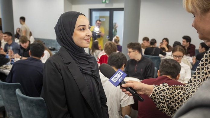 The photo shows a woman wearing a hijab giving an interview.