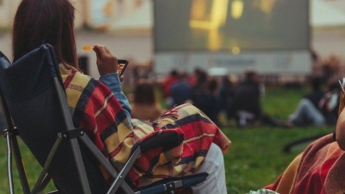 Kobieta siedzi na leżakach i ogląda film kin plenerowego