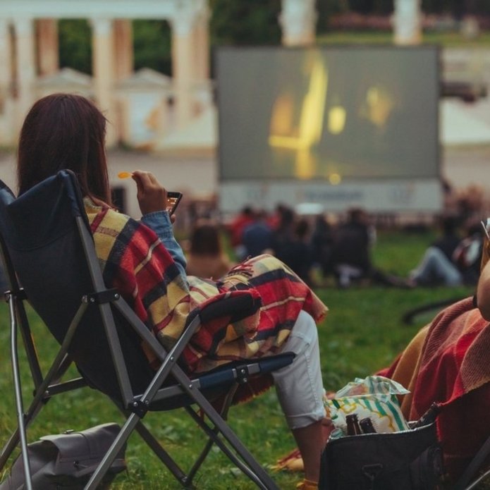 Kobieta siedzi na leżakach i ogląda film kin plenerowego